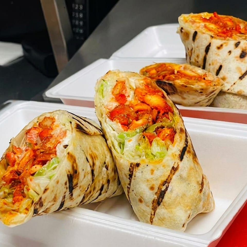 Grilled wraps filled with roasted meat, tomatoes, and lettuce arranged in open white takeout containers.