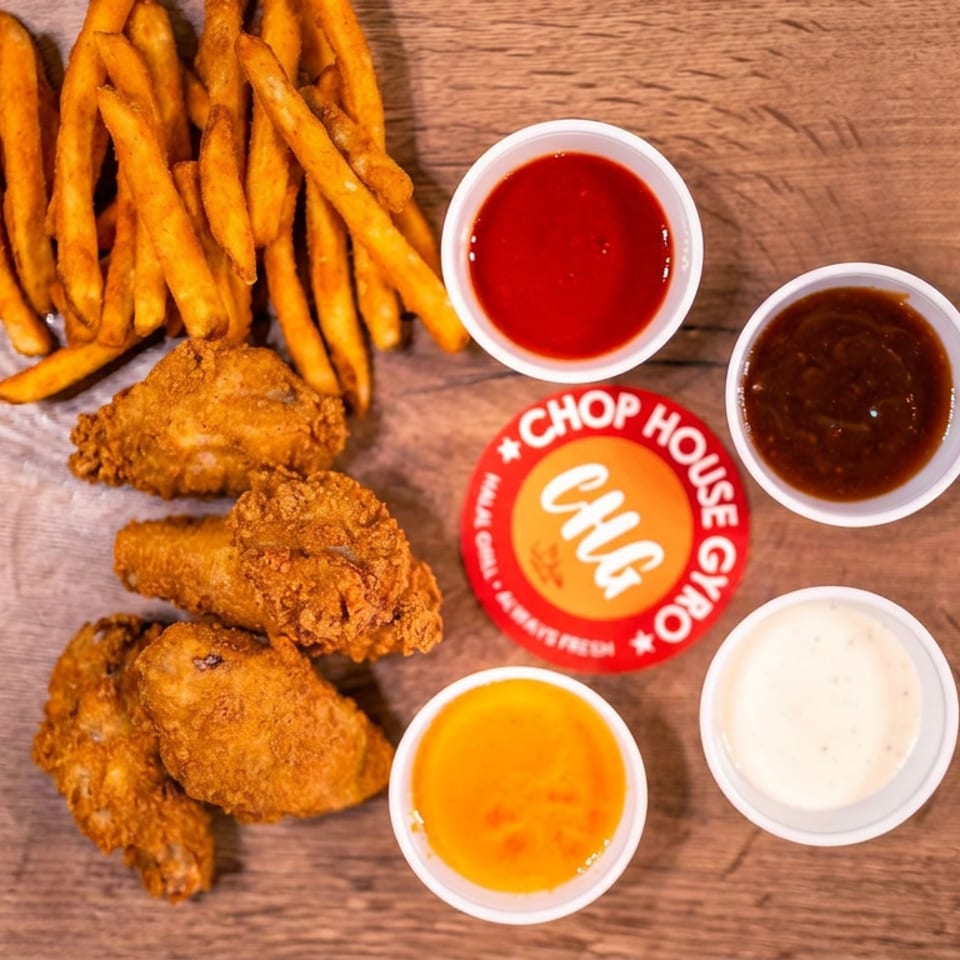 Crispy chicken tenders and sweet potato fries with four dipping sauces on a wooden table beside a Chop House Chicken logo.